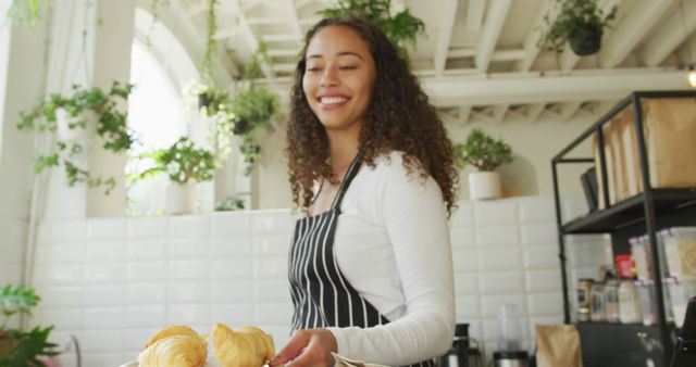 Happy biracial female barista taking croissants on plate from display at cafe. small independent cafe business.