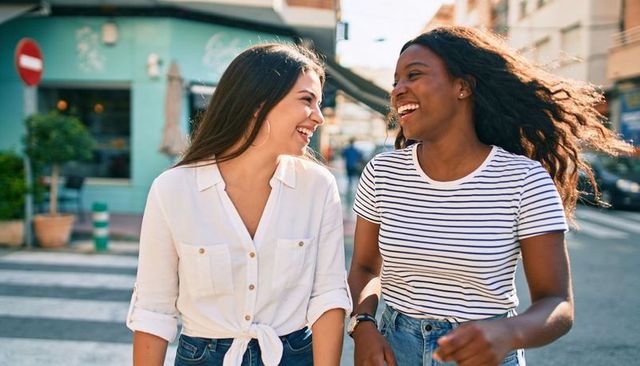 Friends walking and laughing on sunlit urban crosswalk, casual denim lifestyle