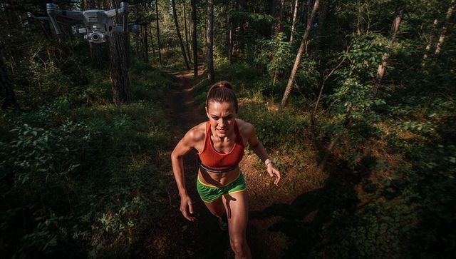 Female Athlete Charging Uphill on Forest Trail with Drone Tracker and Training Gear