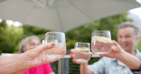 Senior Friends Toasting with Drinks Outdoors Under Umbrella