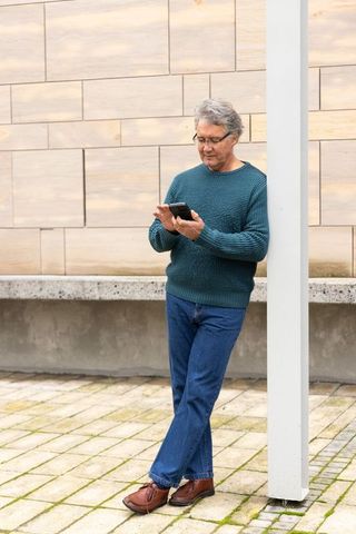Senior man checking smartphone while leaning on column in urban courtyard