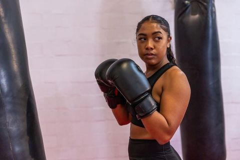 Female boxer training with heavy bag against brick wall, focused athletic workout