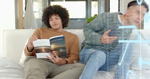 Reclining reader holding paperback while friend sketching on glass for casual brainstorming