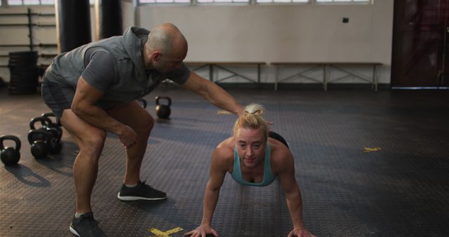 Male trainer correcting form of fit caucasian woman while push up exercise at the gym. sports, training and fitness concept