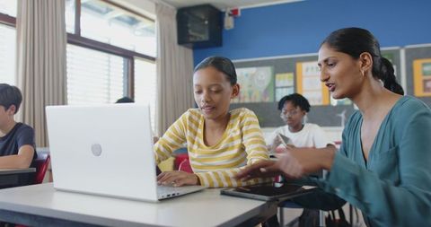 Teacher Assists Student on Laptop in Modern Classroom
