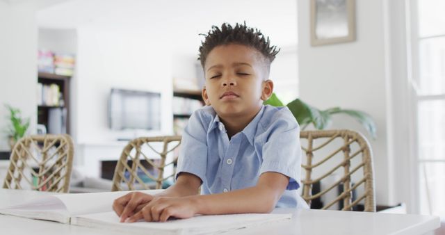 Young boy sits at home table meditating with closed eyes, appearing calm and peaceful. Suitable for themes of childhood mental health, self-care, mindfulness, and relaxation techniques.