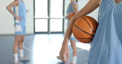 Female Basketball Team Holding Ball at Indoor Gym