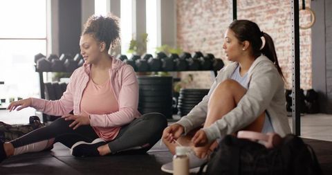 Multiracial women stretching and chatting in gym after workout wearing activewear