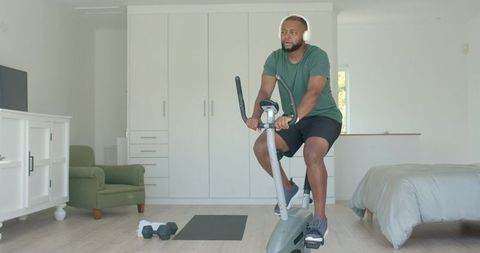 African american man pedaling stationary bike in bedroom for home cardio workout