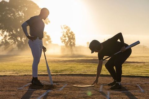 Backlit baseball players adjusting home plate during golden hour practice