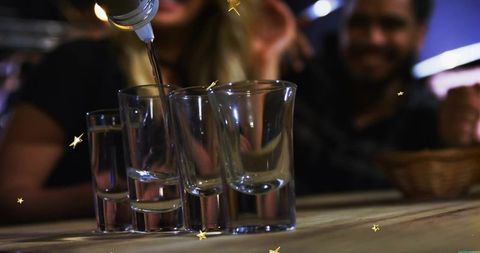 Pouring liquor filling shot glasses on wooden bar counter during social night out