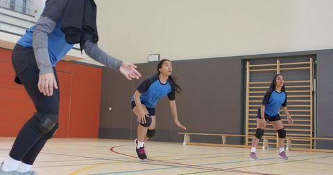 Girls volleyball team lunging and preparing to receive serve in indoor gym training