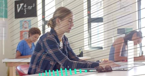 Typing student in plaid shirt working on laptop in bright classroom with sunglasses