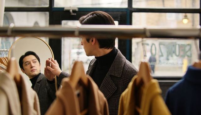 Man checking reflection in oval mirror while shopping coats in urban boutique