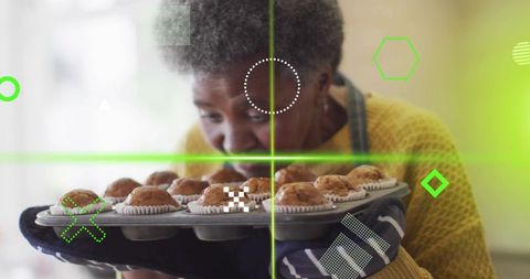 Senior woman smelling fresh muffins while holding muffin tray in cozy sunlit kitchen