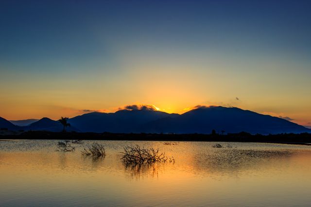 Scenic view of a tranquil lake reflecting the vivid colors of a sunset with distant mountains in the background. Ideal for relaxation themes, travel blogs, nature photography, and wallpaper.