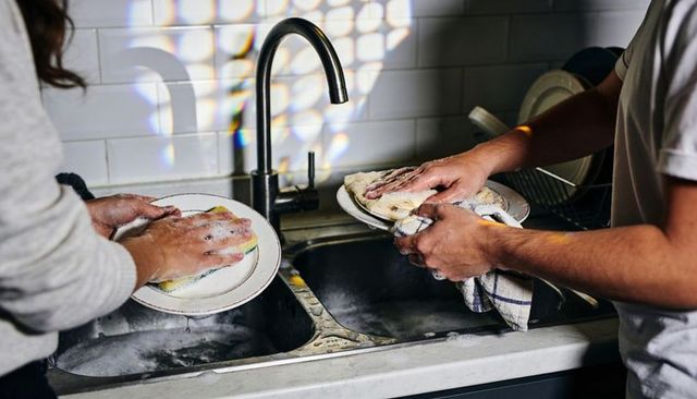 Couple washing dishes together at kitchen sink with sponge, towel and soap suds everyday home life