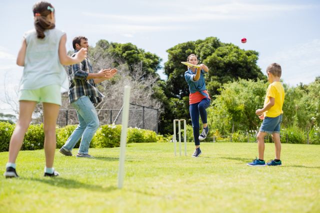 Family playing cricket in park on sunny day. Perfect for depicting family bonding, outdoor activities, summer fun, and sports. Suitable for use in advertisements, brochures, and websites promoting family values, outdoor activities, and recreational sports.