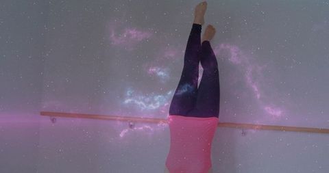 Inverting dancer gripping barre with cosmic nebula overlay for fitness balance studio
