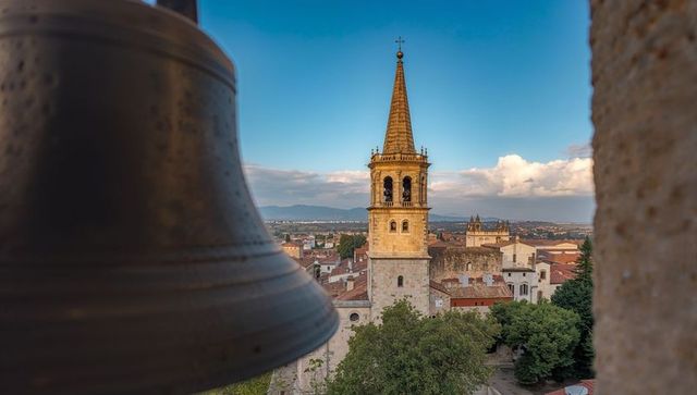 Framing medieval bell tower overlooking red-roof town and cathedral spire at golden hour