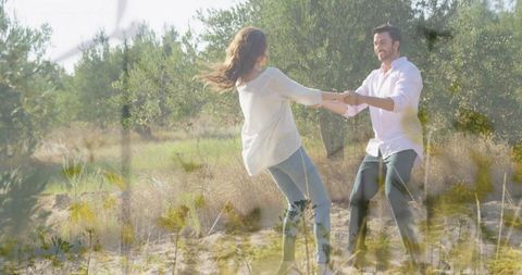 Couple spinning and laughing while holding hands in sunlit olive grove, golden light
