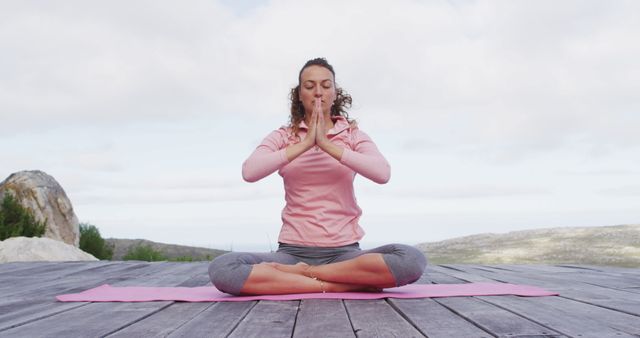 Caucasian woman practicing yoga meditation in lotus position on deck in rural mountainside setting. healthy living, off grid and close to nature.