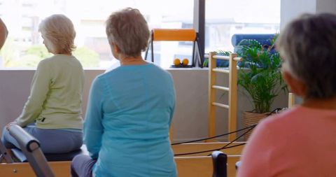 Senior Women Performing Reformer Pilates in Bright Studio Promoting Active Aging Balance