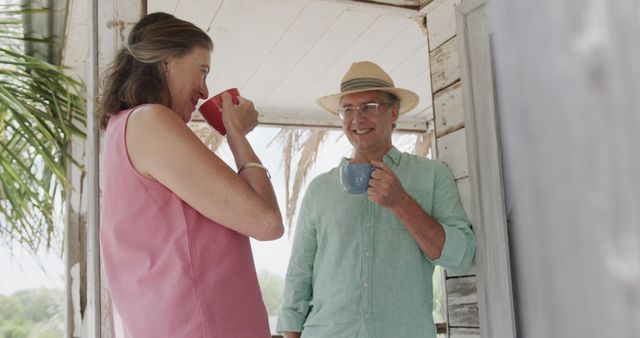 Happy senior caucasian couple drinking coffee outside house on beach. Senior lifestyle, nature, relaxation, vacation, summer and leisure, unaltered.