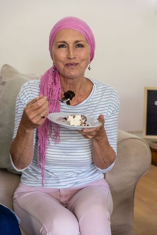Senior woman with pink headscarf enjoying cake at home