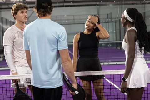 Mixed group of tennis players discussing post-point tactics at net on purple indoor court