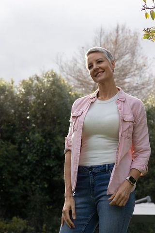 Confident mature woman enjoying peaceful garden moment wearing pink shirt and smartwatch