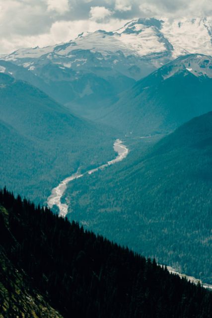 Breathtaking mountain landscape featuring a winding river flowing through the valley, surrounded by forests and snow-capped peaks. Ideal for travel promotions, nature documentaries, outdoor adventure advertisements, and desktop wallpapers.