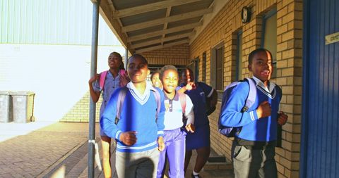 Happy schoolchildren exiting classroom wearing backpacks