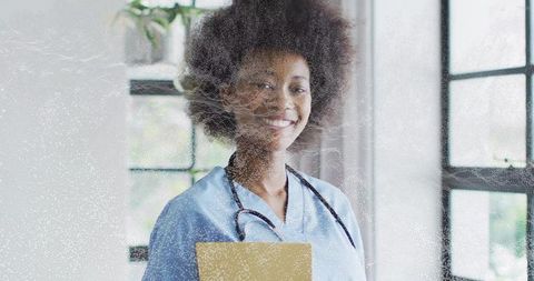 Smiling Nurse in Scrubs Holding Folder in Bright Clinic with Large Windows