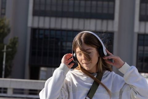 Young woman adjusting wireless headphones on rooftop terrace with urban skyline