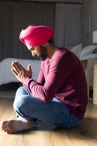 Meditative indian man with pink turban praying in bedroom