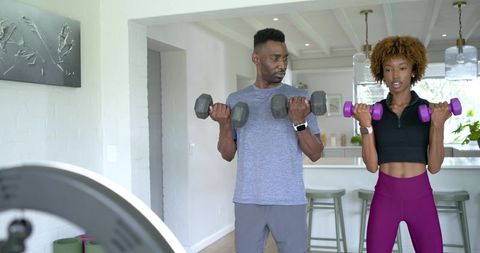 Couple lifting dumbbells in bright kitchen home workout African man and African American woman
