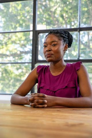 Professional Woman Sitting at Wooden Table in Sunlit Office Setting