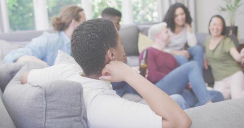Young adult relaxing on sofa listening to friends during casual living room gathering