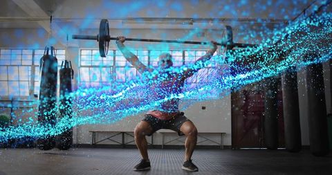Male athlete lifting barbell overhead while squatting with turquoise energy streak in gym