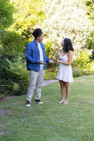Couple sharing rose in sunlit garden conversing during romantic summer moment