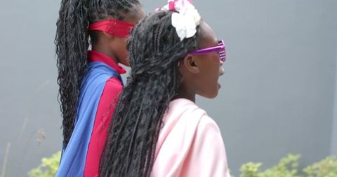 Two girls playing superhero with capes, masks and sunglasses, pretending outdoors