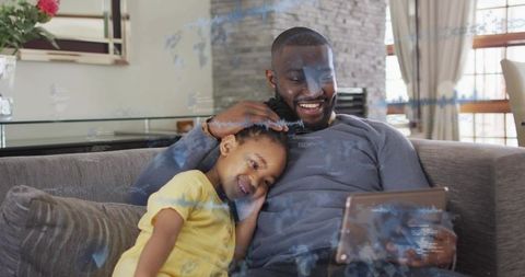 African american father and daughter bonding on tablet, smiling and relaxing on sofa