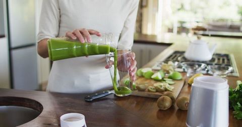 Healthy Living: Woman Pouring Green Smoothie in Kitchen