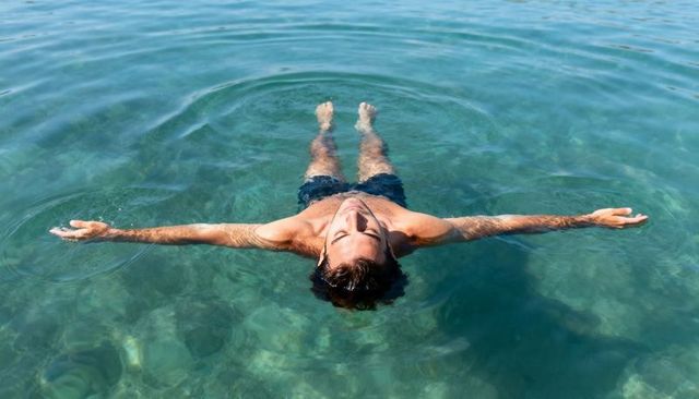 Man floating calmly on sunlit turquoise sea with outstretched arms
