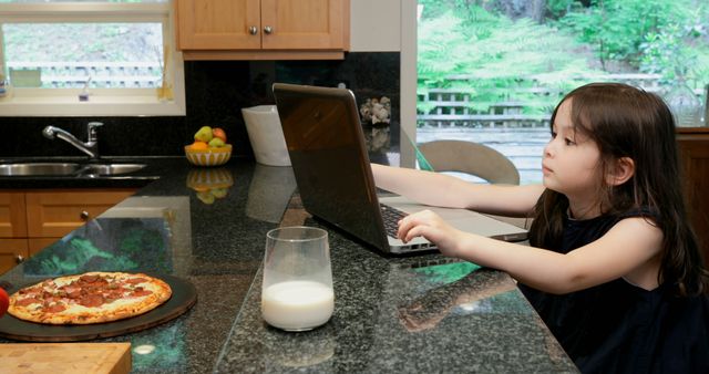 Young girl using laptop in kitchen with pizza and milk on counter - Download Free Stock Images Pikwizard.com