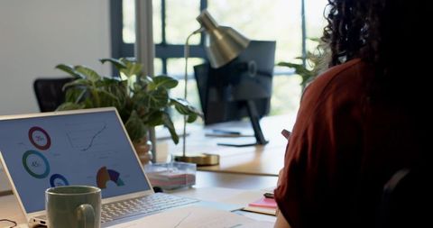 African american woman reviewing analytics on laptop in sunlit office with plants