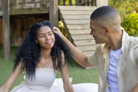 Sunlit backyard couple sharing playful tender moment near wooden playset, summer romance