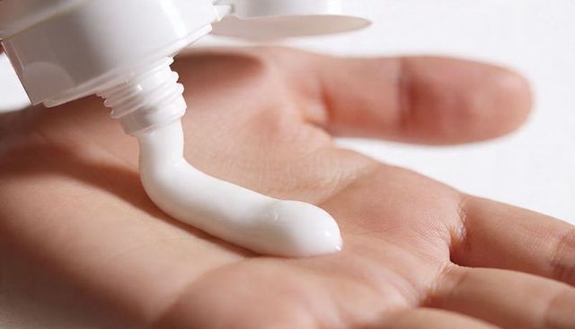 Dispensing white lotion from flip-top squeeze tube onto open palm, closeup skincare concept