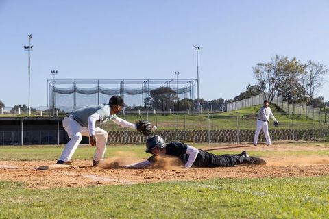 Diving runner sliding into base while fielder reaching to tag during close baseball play